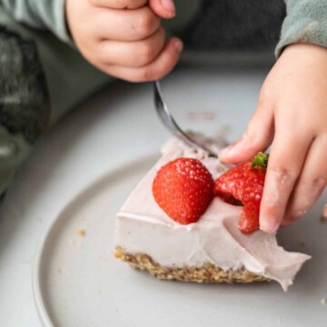 A toddler eating strawberry vegan cheesecake.