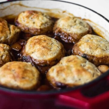 A red casserole dish full of vegan stew with crispy golden dumplings floating on top.