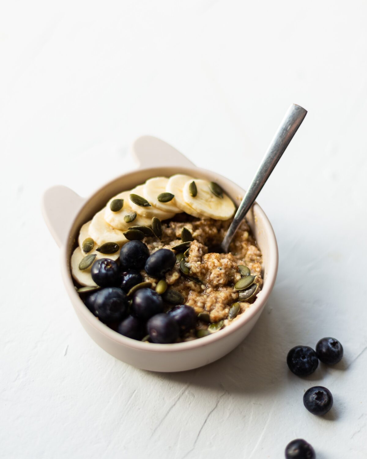 The finished bowl of weetabix based breakfast, topped with fresh blueberries, sliced banana and pumpkin seeds.