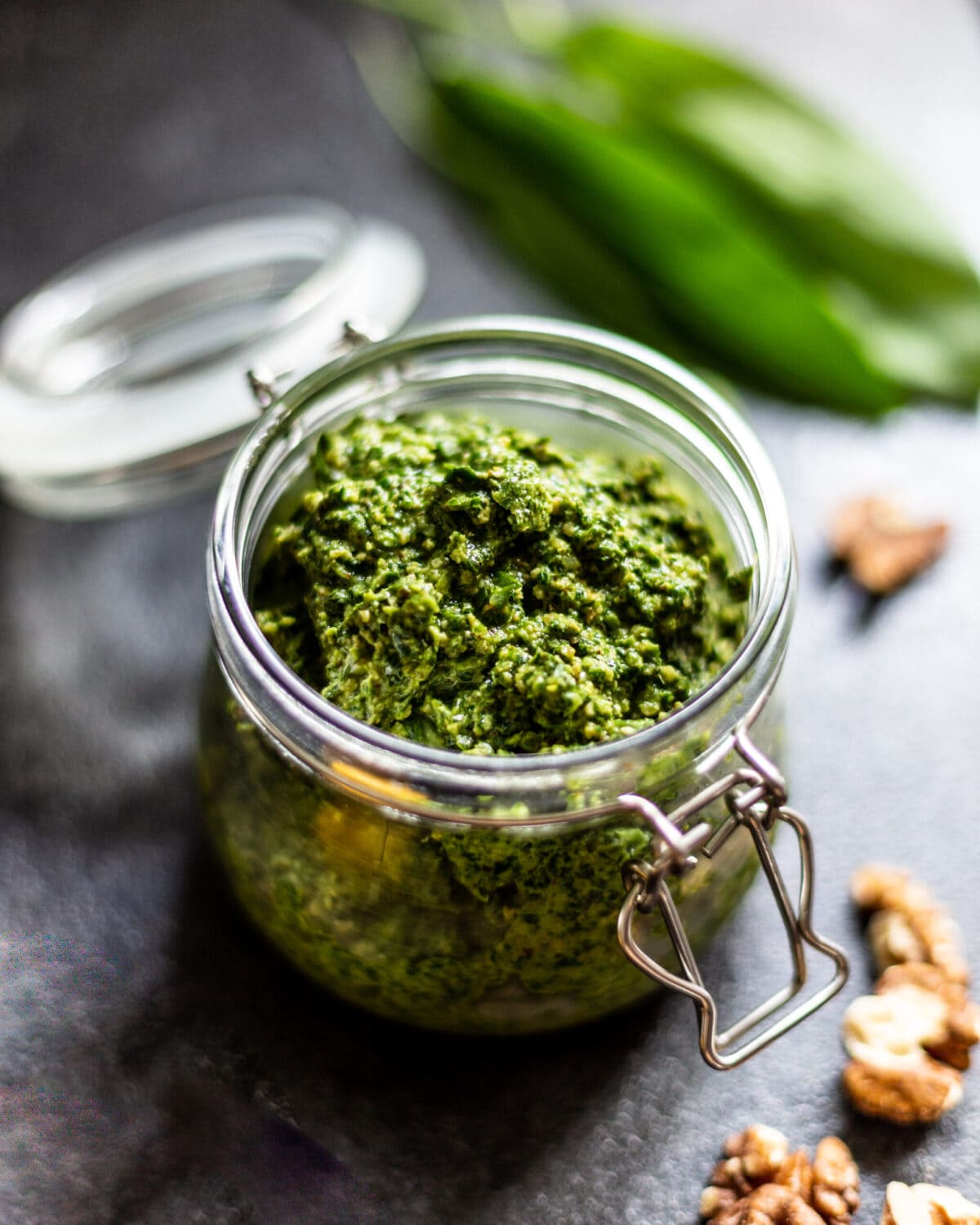 A swing lid jar filled with pesto, surrounded by walnuts and wild garlic leaves.