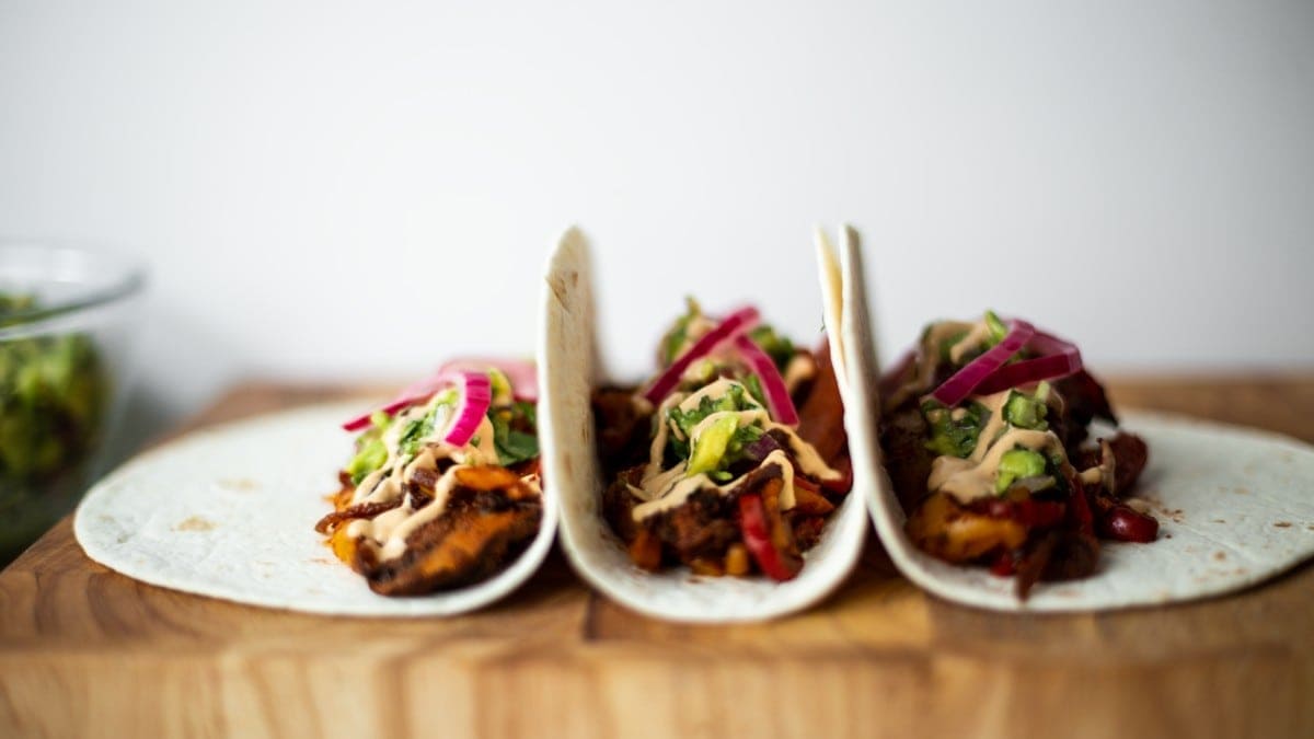 Three filled fajitas stacked side by side on a chopping board. Photographed from the side.