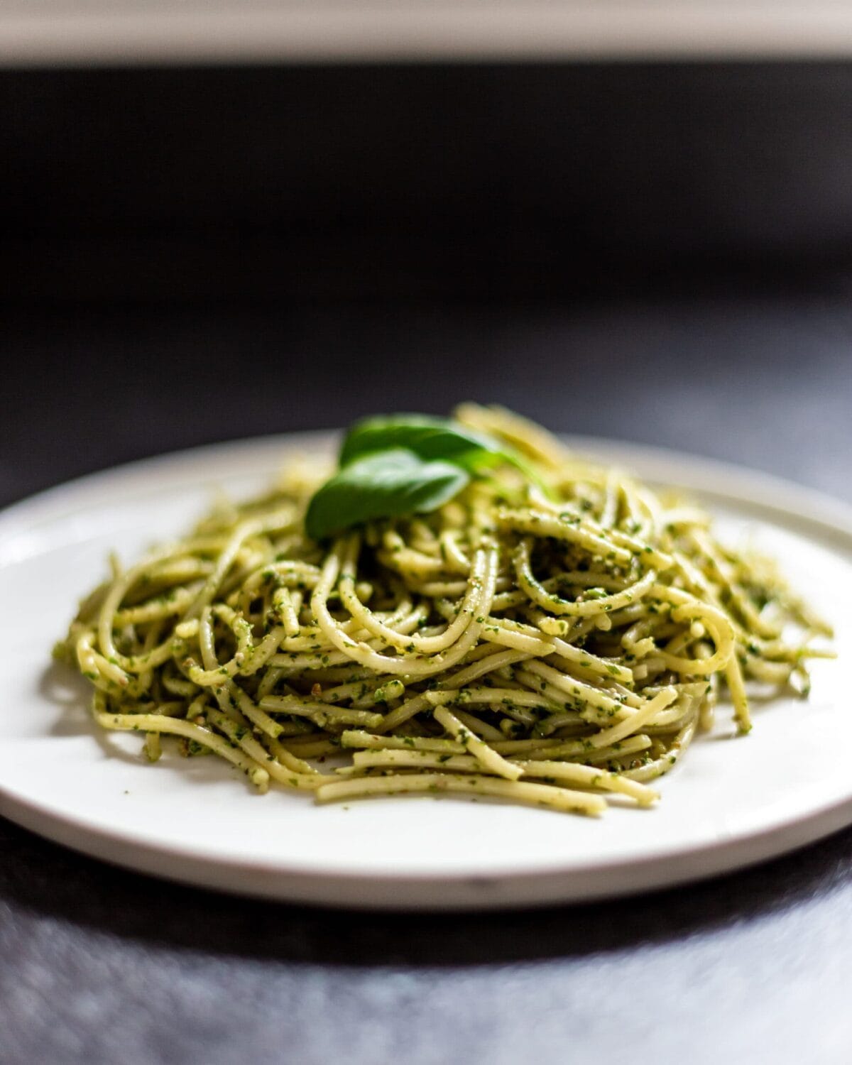 A plate of cooked spaghetti with walnut wild garlic pesto, topped with a basil leaf.