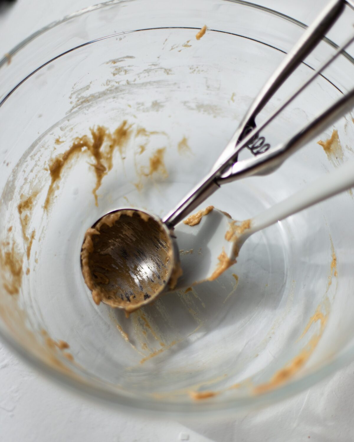A glass bowl with muffin batter remnants, with a spatula and ice cream scoop inside.