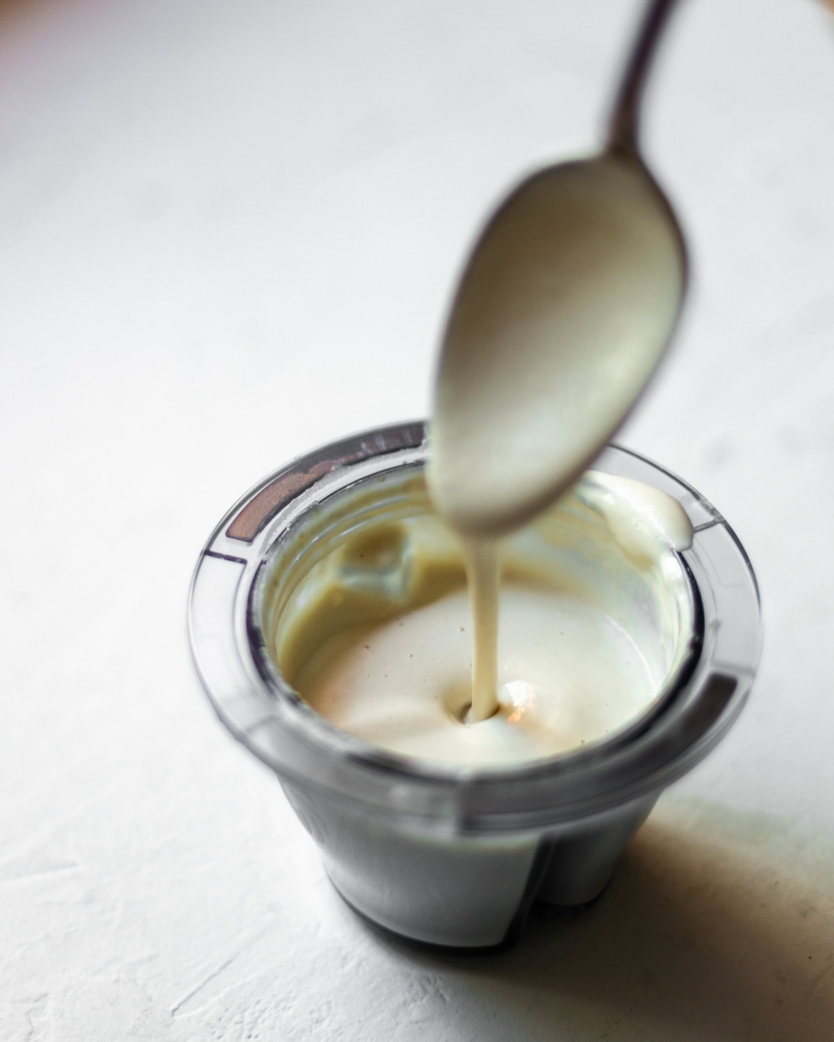 Garlic cashew cream being drizzled from a spoon into a bowl.