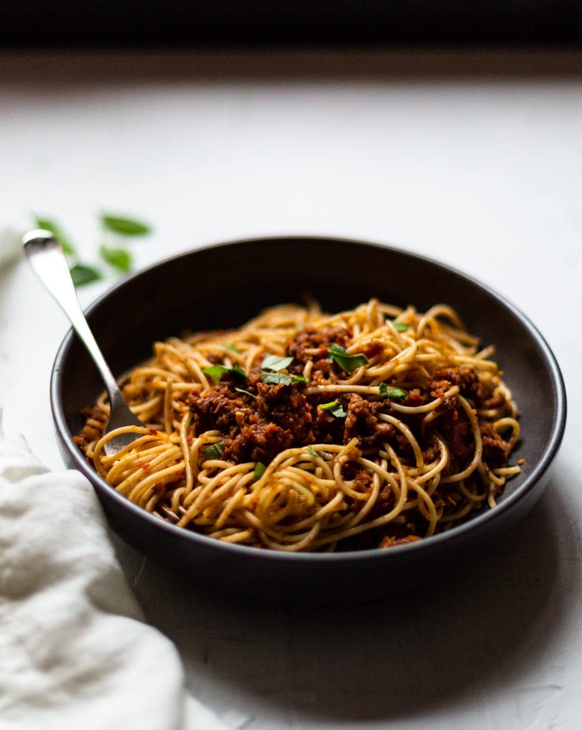 A dark grey bowl filled with lentil and mushroom bolognese, topped with fresh chopped basil.