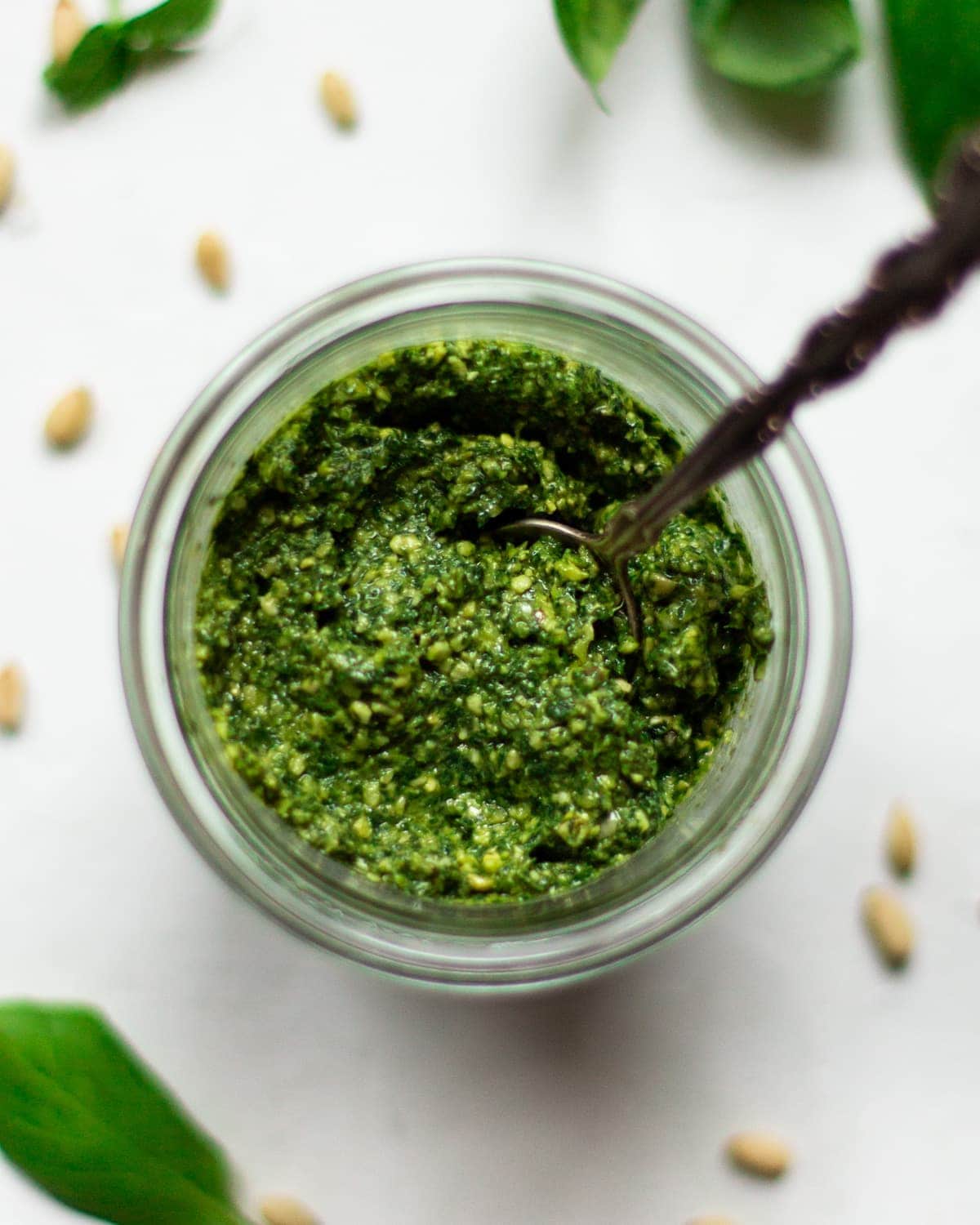 An overhead photo of the vegan pesto in a glass jar on a white background.