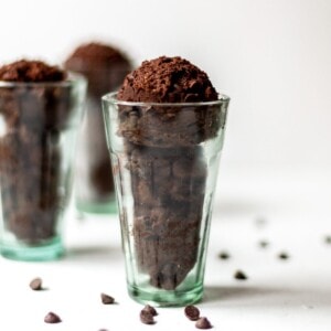 Three scoops of double chocolate cookie dough in a tall glass, made to look like ice cream, on a white background with scattered chocolate chips in the foreground.
