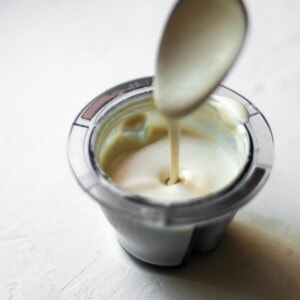 Garlic cashew cream being drizzled from a spoon into a bowl.