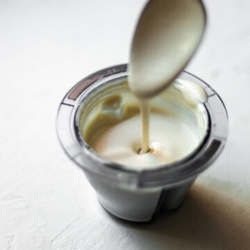 Garlic cashew cream being drizzled from a spoon into a bowl.