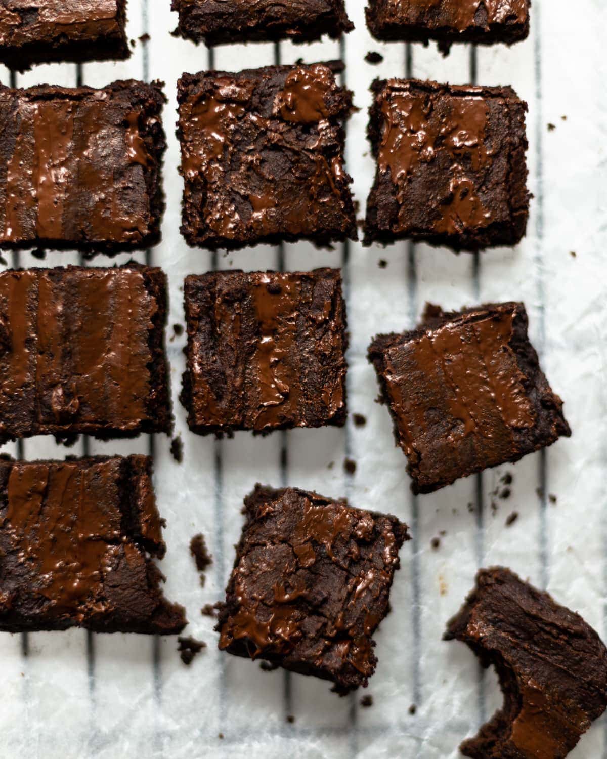 An overhead image of the vegan blackbean brownies on white baking paper, on a black cooling rack.