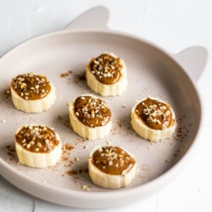 Banana slices on a plate, covered with almond butter, cinnamon and hemp seeds.