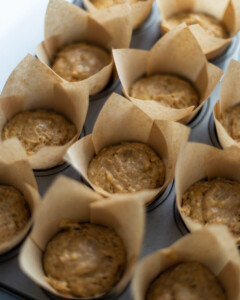 The uncooked batter, portioned out into the muffin cases, in a muffin tray.
