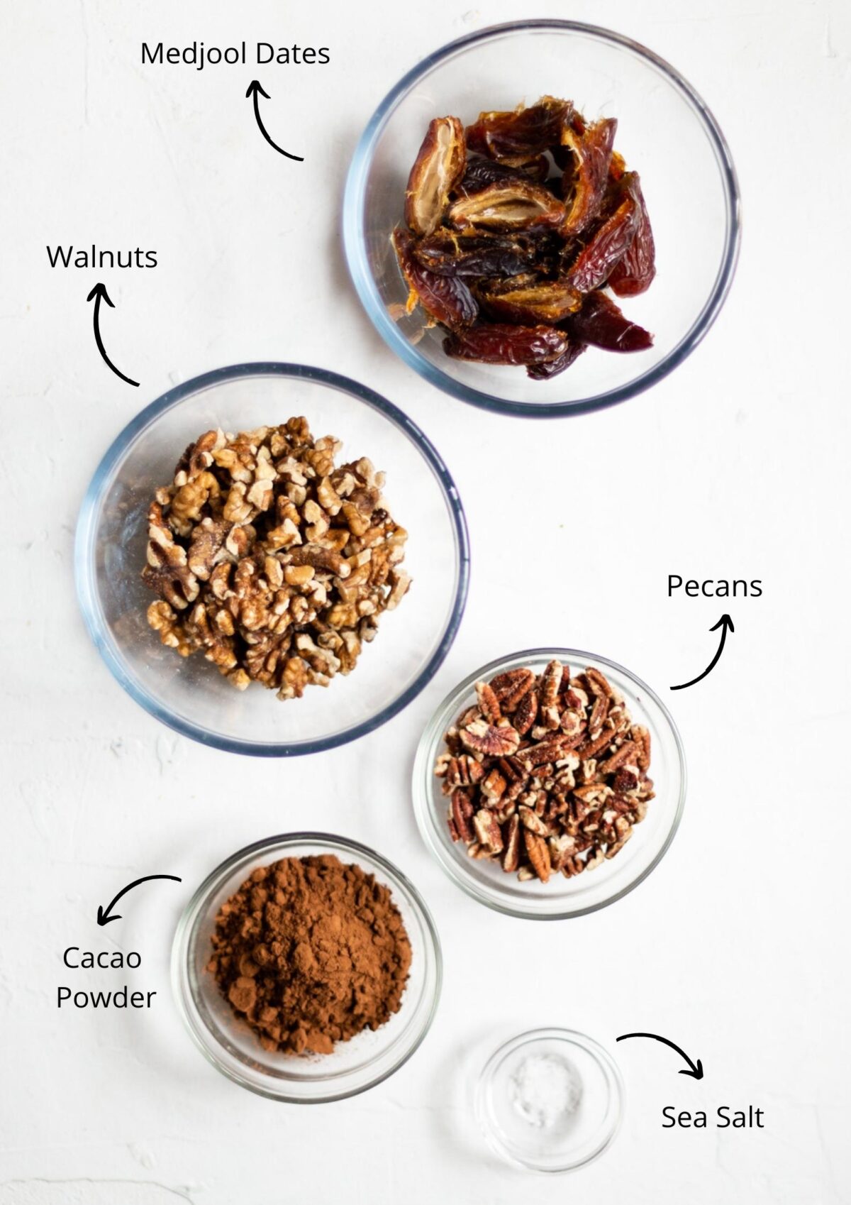 Overhead photo of the vegan caramel slices base ingredients. All in glass bowls, on a white background.