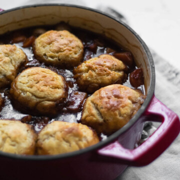 A red casserole dish full of vegan stew, with golden dumplings floating on the top.