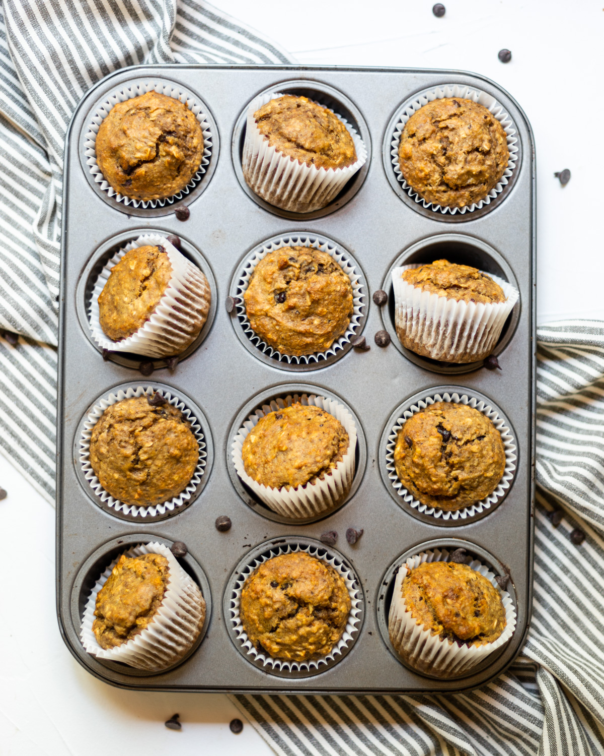 An oven tray of cooked muffins on a grey striped linen cloth.