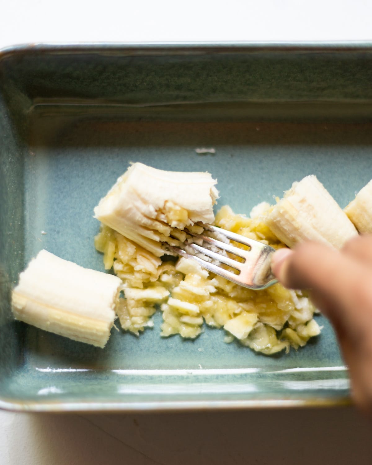 The banana being mashed with a fork, in the ovenproof dish.