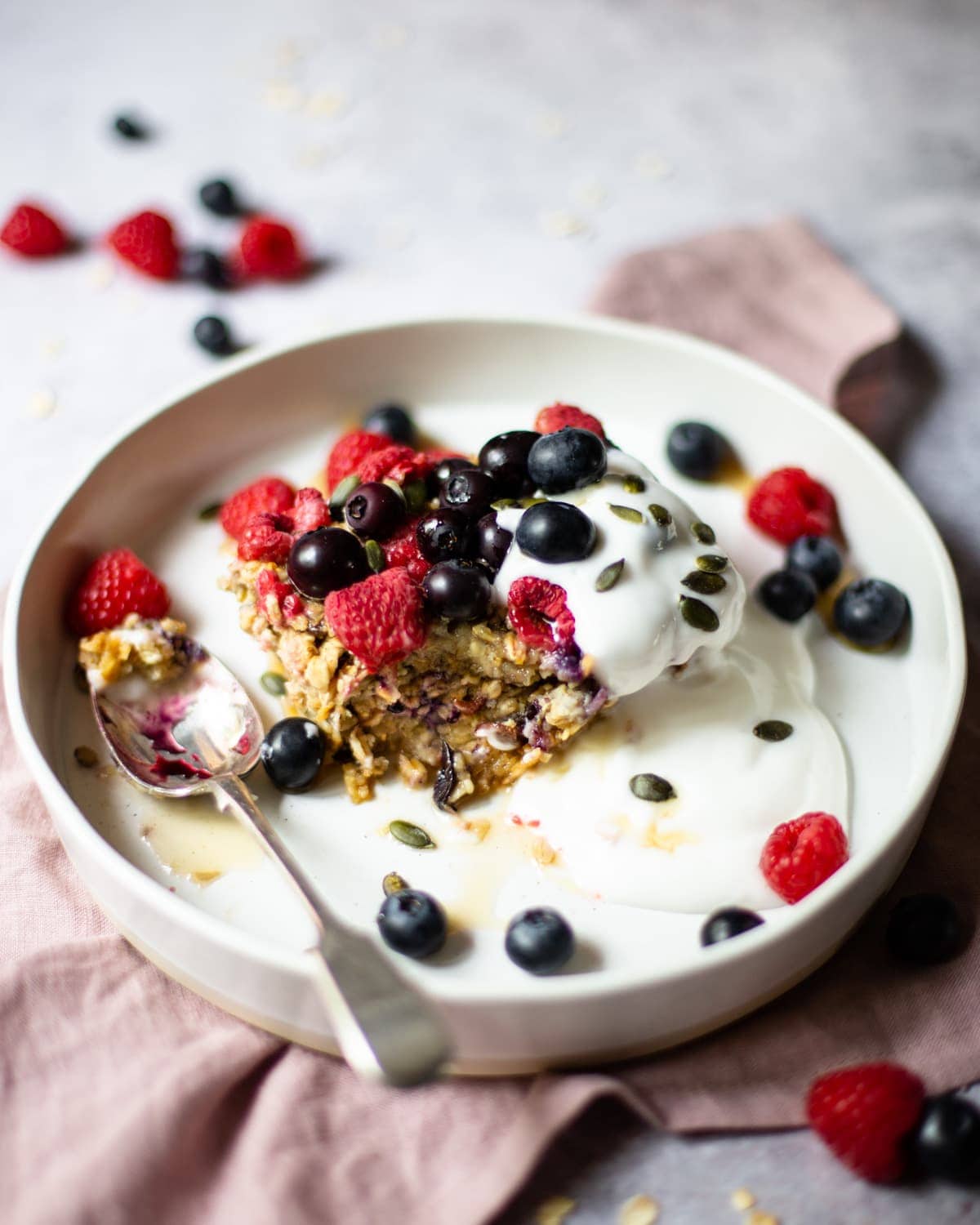 A bowl of baked oats, topped with extra fresh berries, coconut yoghurt, pumpkin seeds and maple syrup.