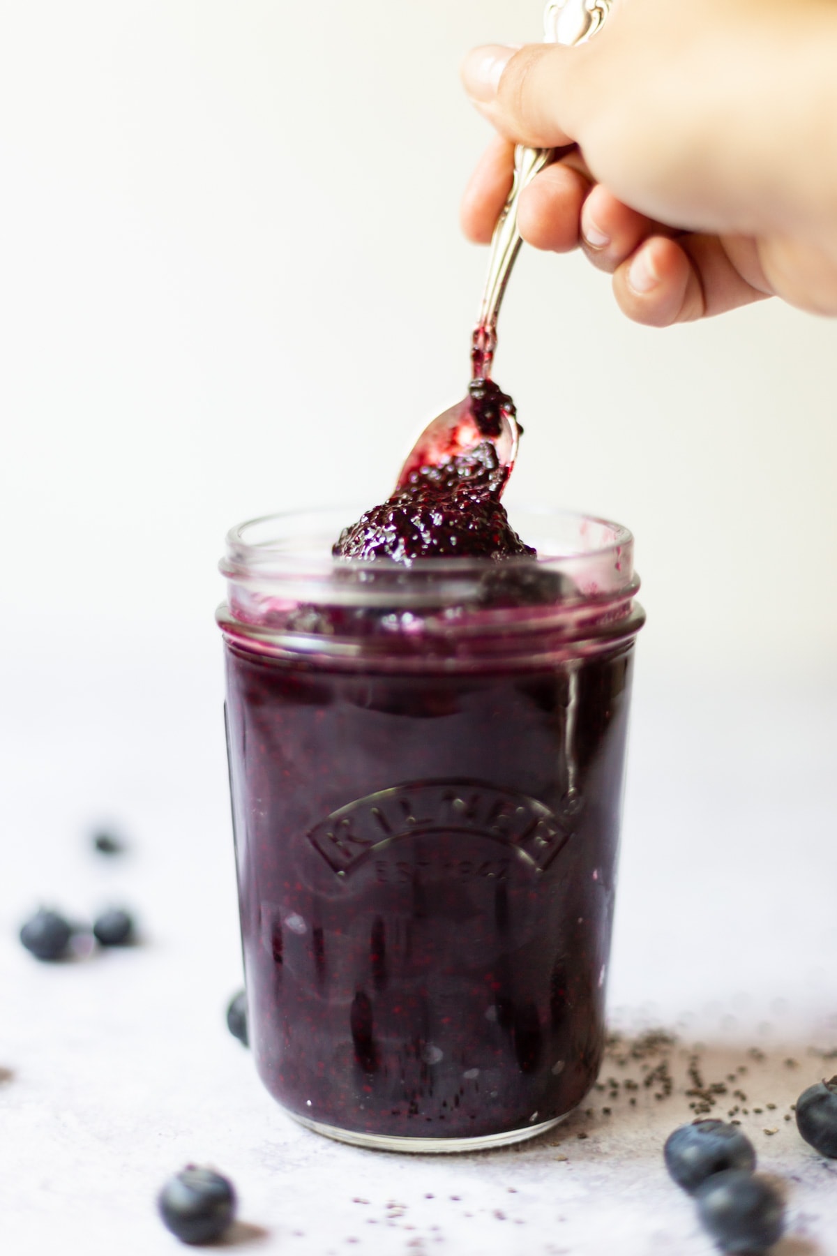 A jar of blueberry jam with a spoonful of it being taken out.