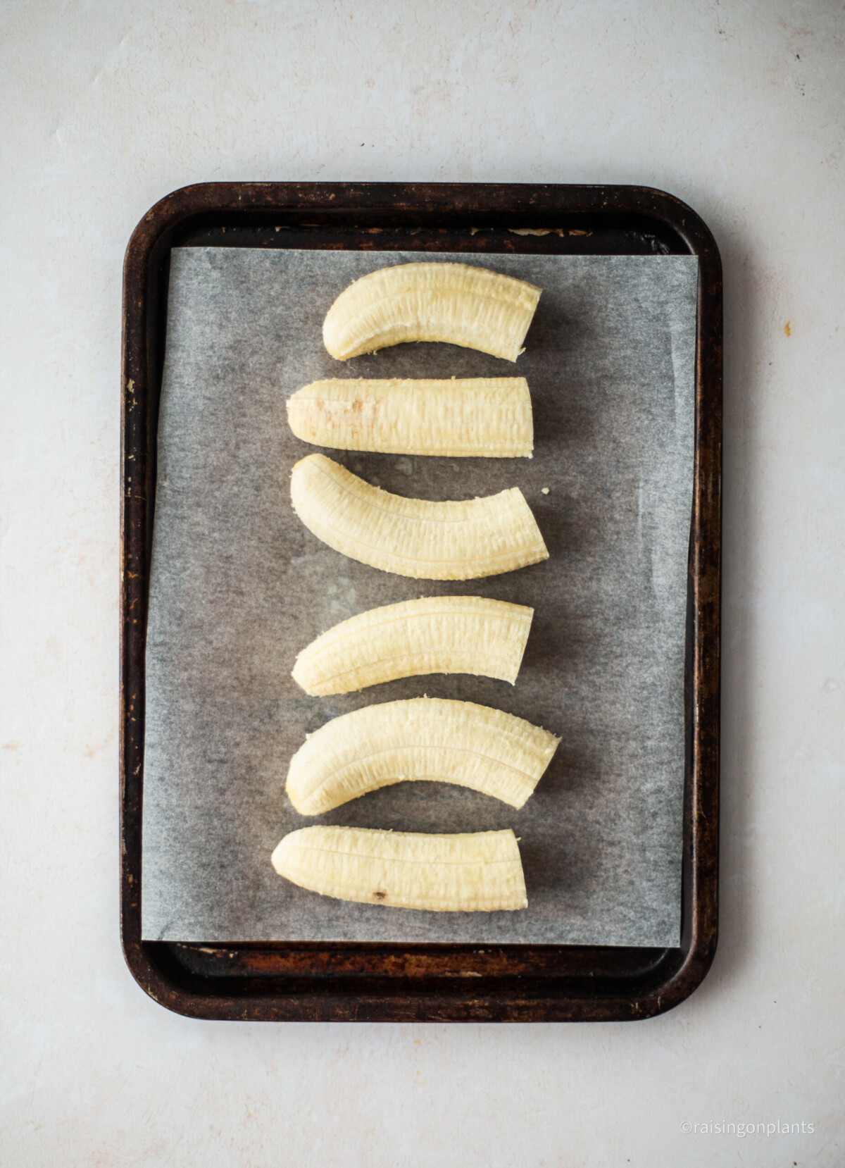 Three bananas cut in half and laid on a baking tray lined with baking paper.