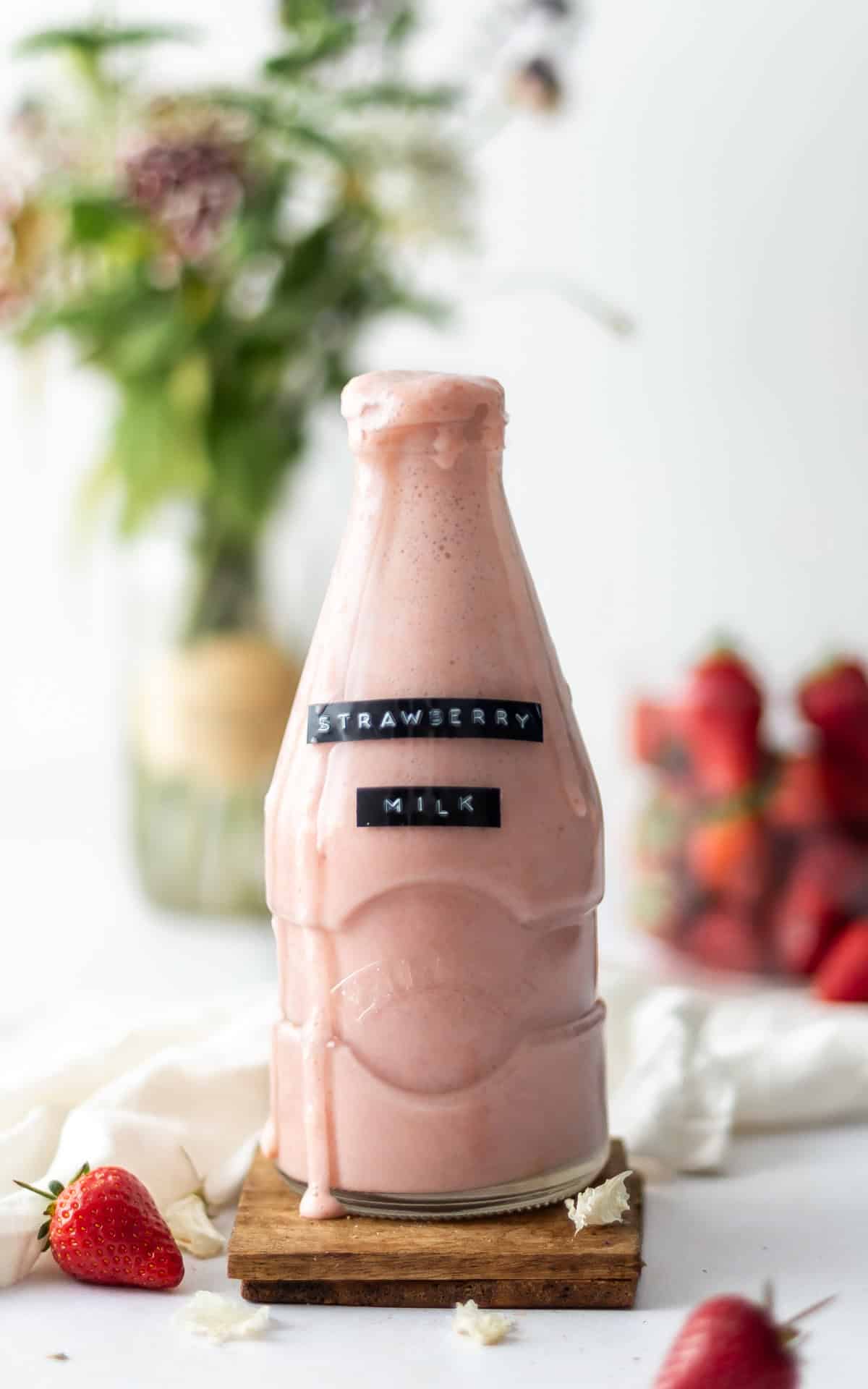 A milk bottle filled with strawberry almond milk, with a little overflowing down the front.